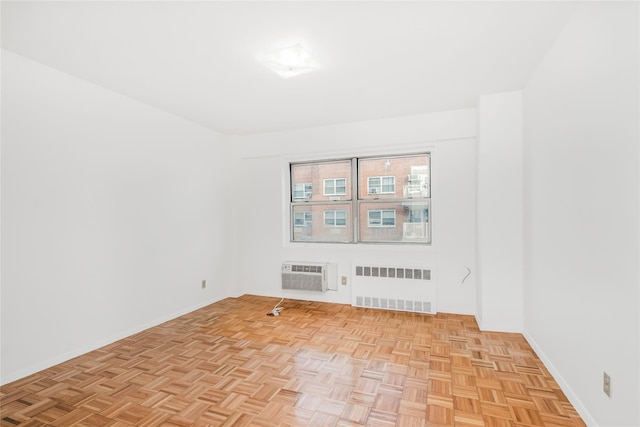 spare room with radiator heating unit, a wall unit AC, and light parquet flooring