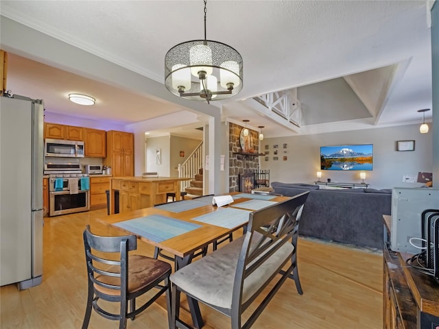 dining area with crown molding, a notable chandelier, a fireplace, and light hardwood / wood-style flooring