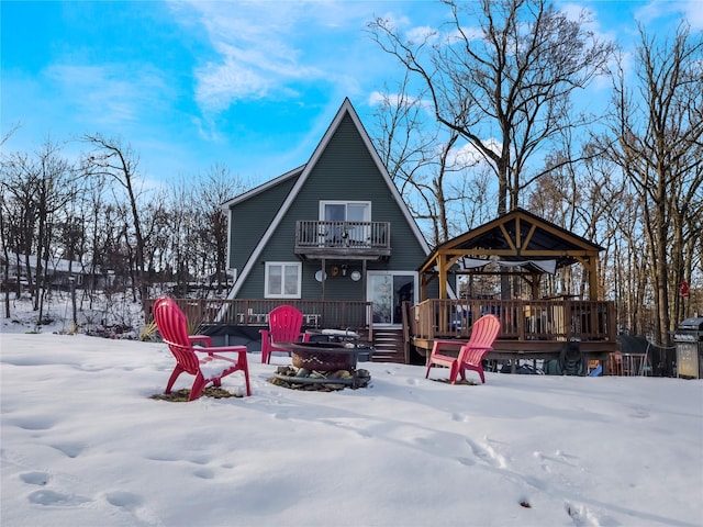 snow covered house with a gazebo, a balcony, a deck, and a fire pit