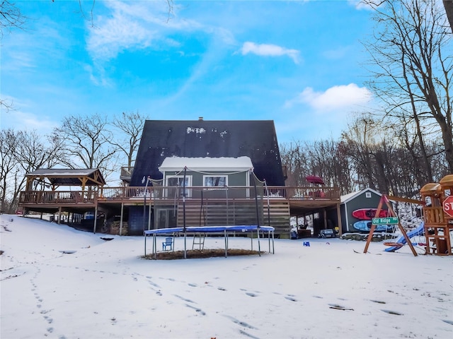 snow covered back of property with a playground, a gazebo, a deck, and a trampoline