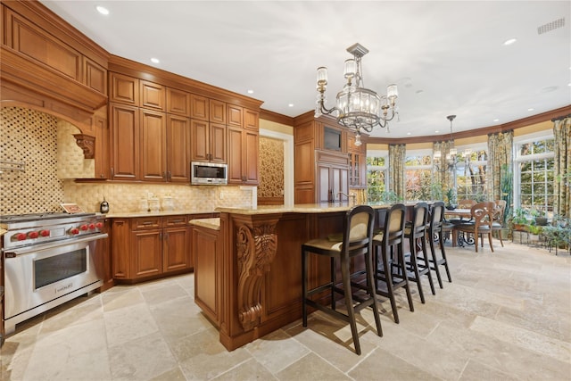 kitchen with light stone counters, a chandelier, hanging light fixtures, stainless steel appliances, and a kitchen island with sink