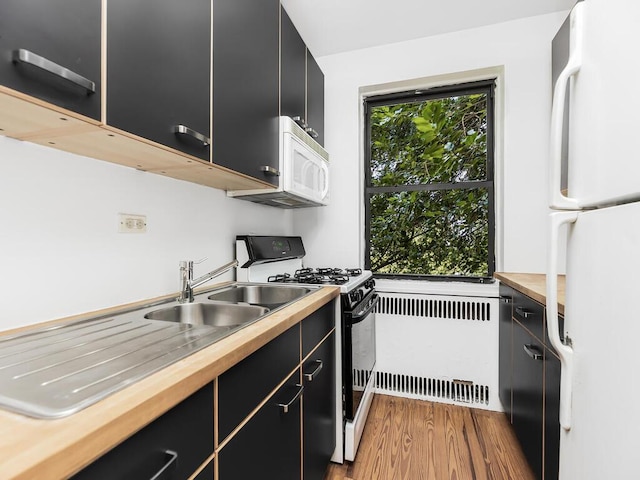 kitchen featuring sink, radiator heating unit, white appliances, and light hardwood / wood-style floors