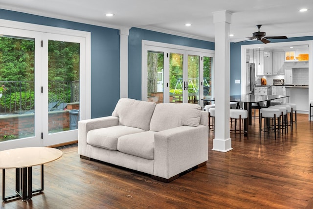 living room with dark wood-type flooring, ceiling fan, ornamental molding, and decorative columns