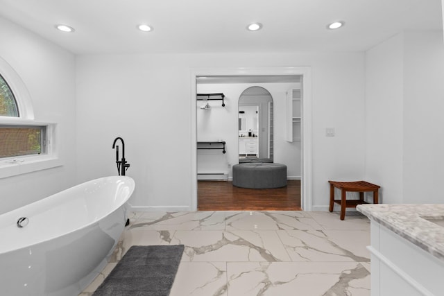 bathroom with baseboard heating, a tub to relax in, and vanity