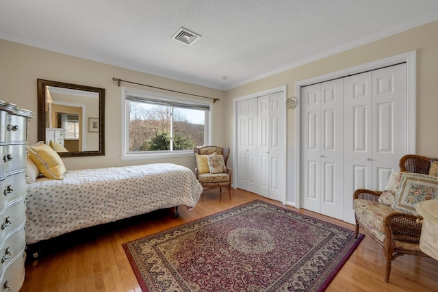 bedroom with hardwood / wood-style flooring, ornamental molding, a textured ceiling, and two closets