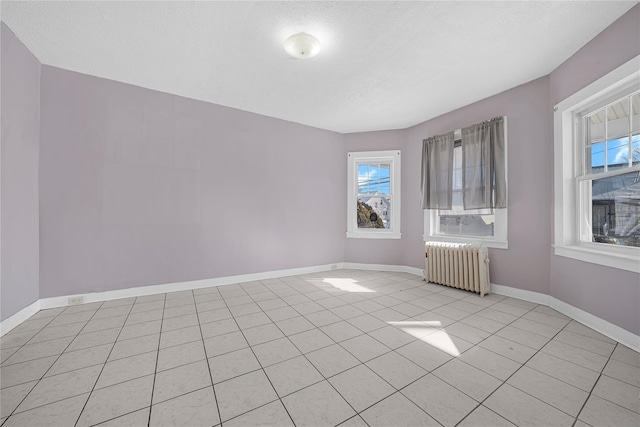 empty room featuring radiator, a wealth of natural light, and light tile patterned flooring