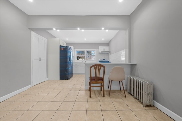 kitchen with black refrigerator, radiator heating unit, white cabinets, a kitchen breakfast bar, and decorative backsplash