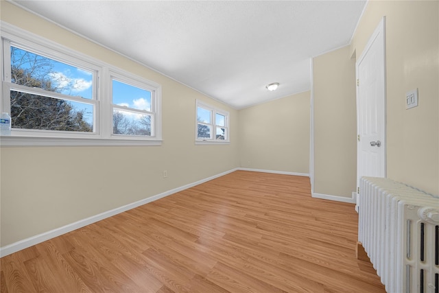 unfurnished room featuring lofted ceiling, radiator, and light wood-type flooring