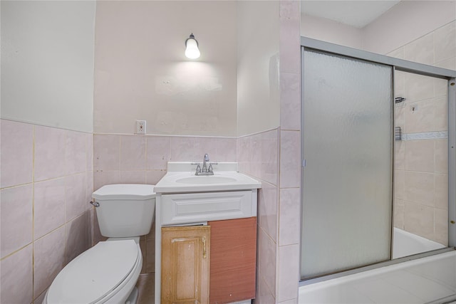 full bathroom featuring vanity, combined bath / shower with glass door, tile walls, and toilet