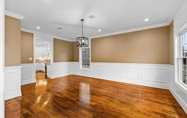 unfurnished dining area featuring hardwood / wood-style floors, crown molding, and a notable chandelier