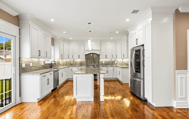 kitchen with pendant lighting, stainless steel appliances, a center island, light stone counters, and white cabinets