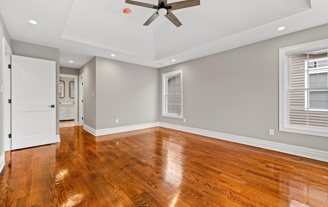 unfurnished room featuring ceiling fan, wood-type flooring, and a raised ceiling