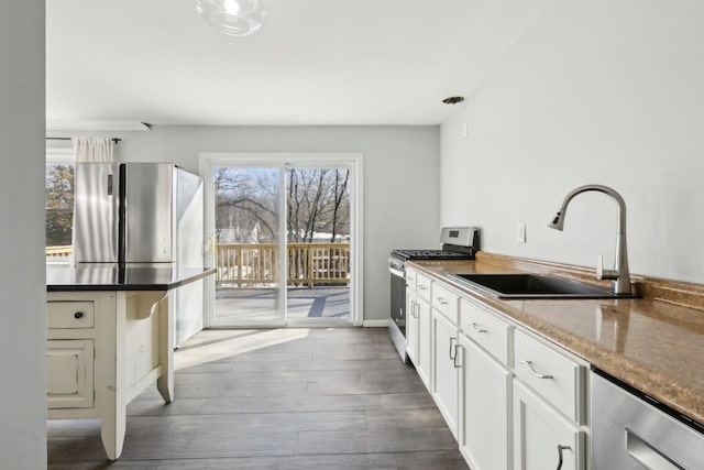 kitchen featuring sink, stone counters, appliances with stainless steel finishes, wood-type flooring, and white cabinets