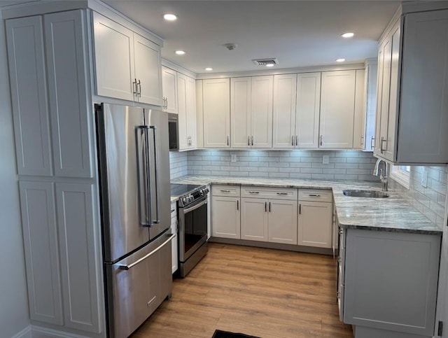 kitchen featuring sink, light hardwood / wood-style flooring, stainless steel appliances, light stone countertops, and white cabinets