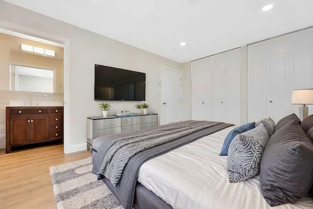 bedroom with light hardwood / wood-style floors, multiple closets, and sink