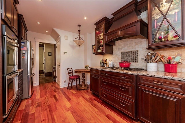 kitchen featuring premium range hood, appliances with stainless steel finishes, pendant lighting, decorative backsplash, and light stone counters