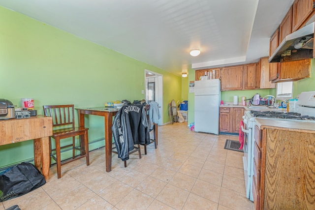 20 E Pine St, Long Beach, NY 11561 - kitchen with white appliances, under cabinet range hood, brown cabinets, light tile patterned flooring, and light countertops