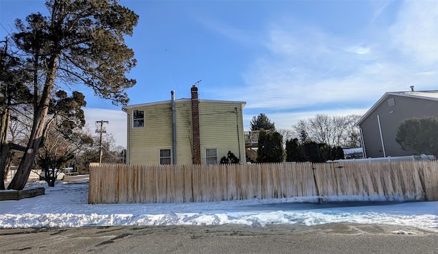 snow covered property featuring a chimney and fence