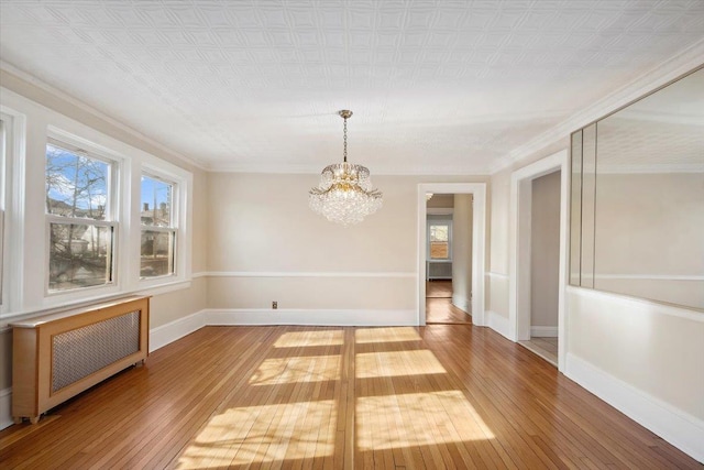 empty room with hardwood / wood-style flooring, ornamental molding, radiator, and a chandelier