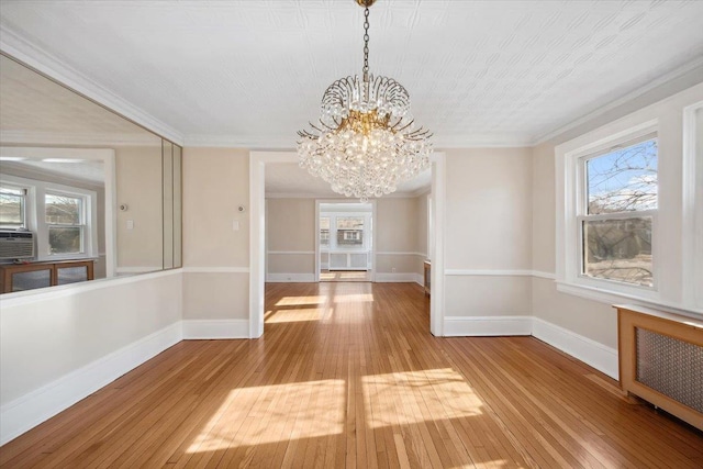 unfurnished dining area featuring hardwood / wood-style floors, crown molding, radiator heating unit, and a chandelier