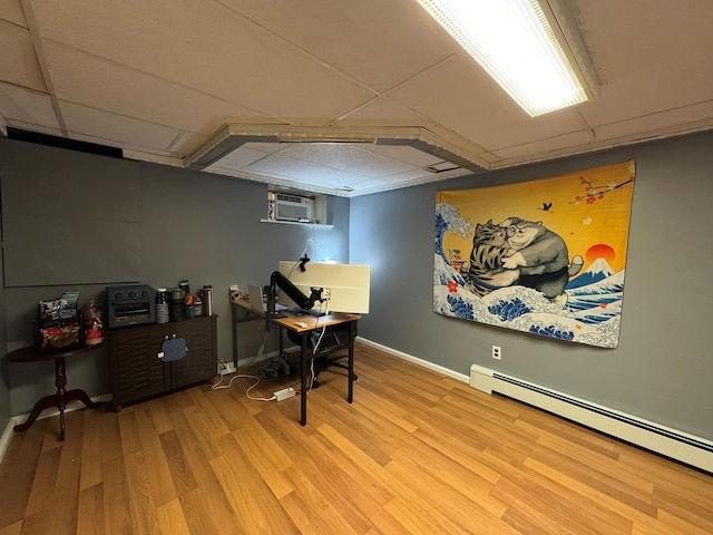 office space with a baseboard radiator, a wall mounted AC, light hardwood / wood-style flooring, and a drop ceiling