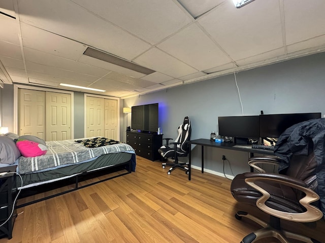 bedroom with light wood-type flooring and a drop ceiling