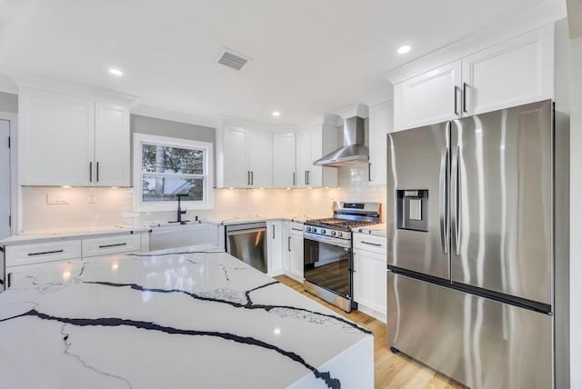 kitchen with wall chimney exhaust hood, appliances with stainless steel finishes, light stone countertops, and white cabinets