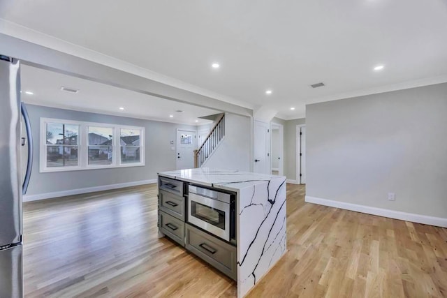 kitchen featuring gray cabinets, a kitchen island, stainless steel appliances, light stone countertops, and light hardwood / wood-style flooring