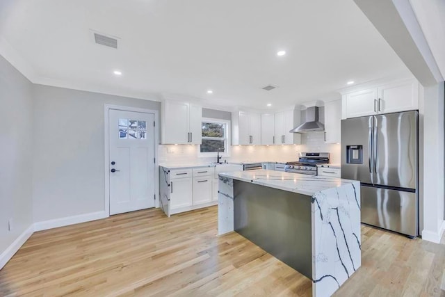 kitchen featuring appliances with stainless steel finishes, white cabinetry, a center island, light stone countertops, and wall chimney exhaust hood