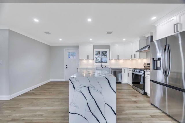 kitchen with wall chimney exhaust hood, tasteful backsplash, light stone counters, stainless steel appliances, and white cabinets