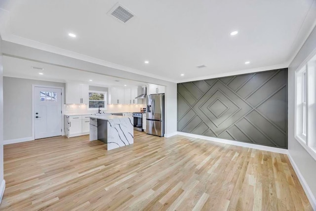 kitchen with a kitchen island, white cabinetry, stainless steel appliances, wall chimney range hood, and light hardwood / wood-style flooring