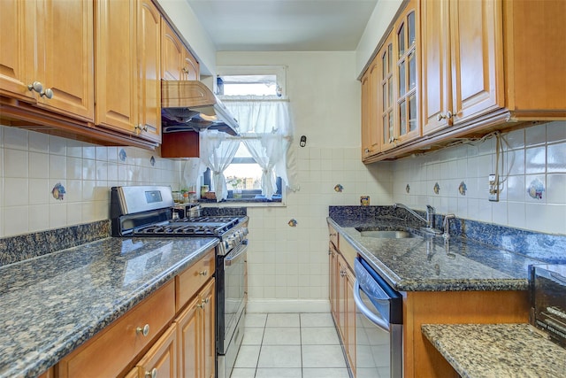 kitchen with appliances with stainless steel finishes, sink, dark stone countertops, exhaust hood, and light tile patterned floors