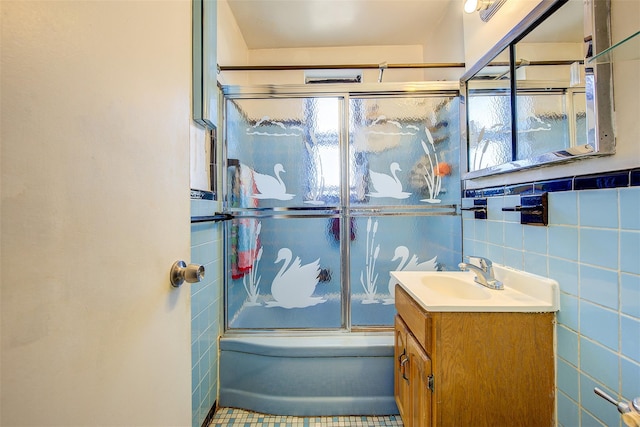 bathroom with tile walls, vanity, and bath / shower combo with glass door