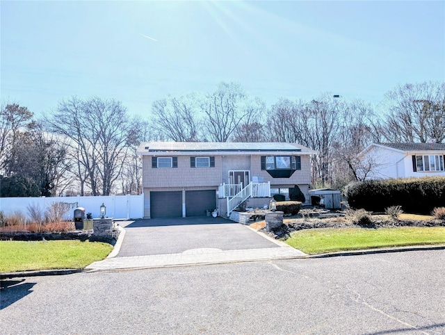 raised ranch with a garage, driveway, and fence