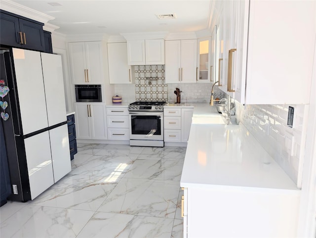 kitchen featuring marble finish floor, light countertops, freestanding refrigerator, stainless steel gas stove, and white cabinetry