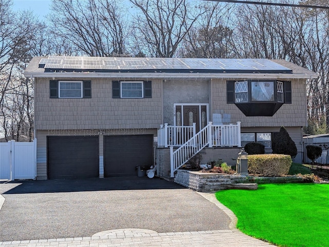 bi-level home featuring solar panels, aphalt driveway, an attached garage, and fence