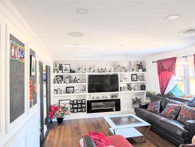 living area featuring built in features, crown molding, visible vents, a glass covered fireplace, and wood finished floors