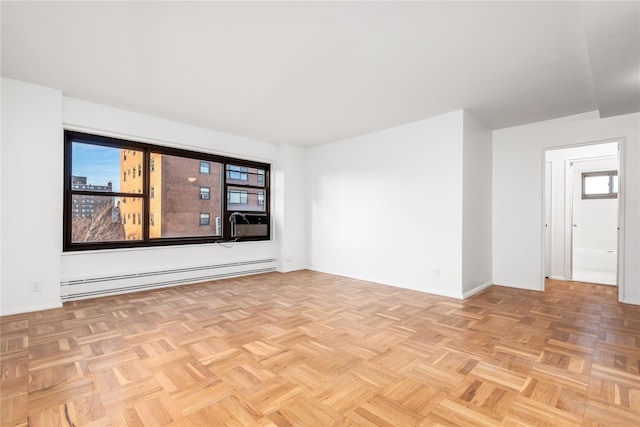 empty room featuring light parquet floors, a baseboard heating unit, and a wealth of natural light