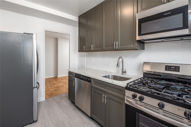 kitchen featuring sink, backsplash, stainless steel appliances, light stone counters, and light parquet flooring