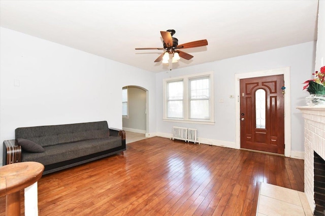 living room featuring a brick fireplace, radiator, hardwood / wood-style floors, and ceiling fan