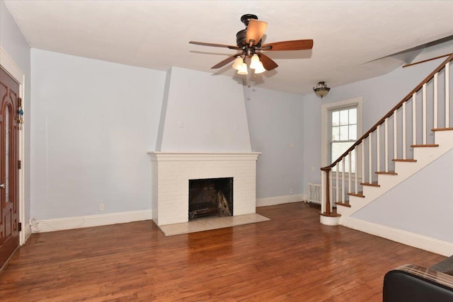 unfurnished living room with a brick fireplace, radiator heating unit, dark hardwood / wood-style floors, and ceiling fan