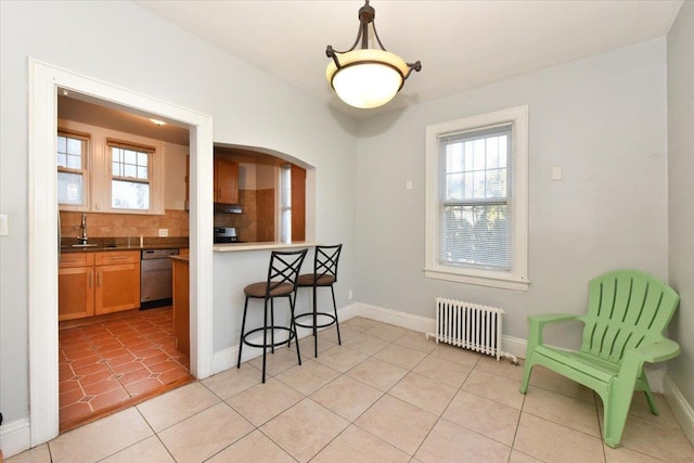 kitchen featuring light tile patterned flooring, a breakfast bar, radiator heating unit, dishwasher, and decorative backsplash