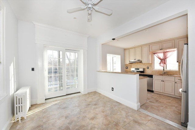 kitchen featuring appliances with stainless steel finishes, radiator, backsplash, ceiling fan, and kitchen peninsula