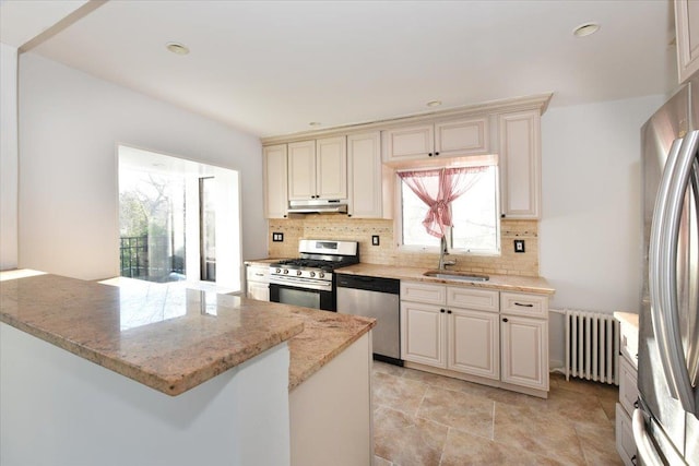 kitchen with radiator, cream cabinets, sink, stainless steel appliances, and light stone countertops