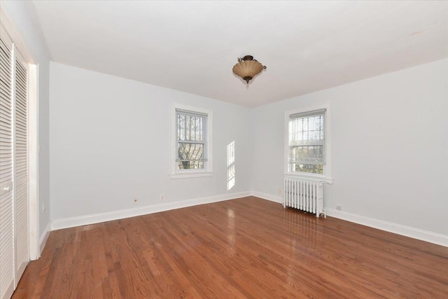 unfurnished bedroom with radiator heating unit, hardwood / wood-style floors, and multiple windows