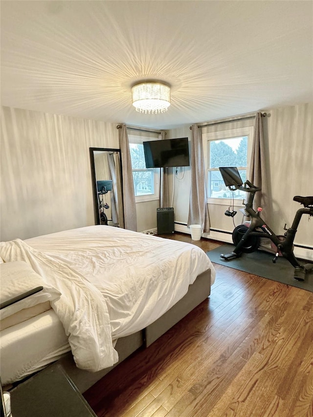 bedroom with multiple windows, a baseboard heating unit, and hardwood / wood-style floors