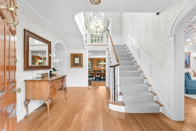 entrance foyer with ornate columns, ornamental molding, light hardwood / wood-style floors, and a notable chandelier