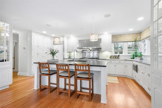 kitchen featuring appliances with stainless steel finishes, pendant lighting, white cabinets, a center island, and wall chimney range hood