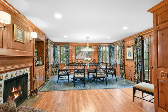 dining space with light hardwood / wood-style flooring, a premium fireplace, a healthy amount of sunlight, and wood walls