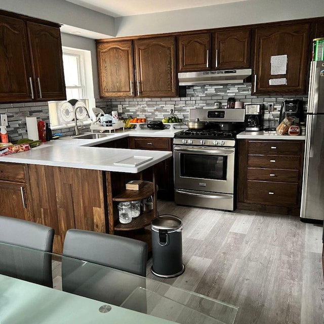 kitchen with appliances with stainless steel finishes, sink, kitchen peninsula, dark brown cabinets, and light hardwood / wood-style flooring